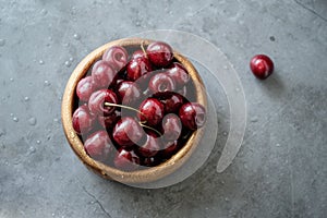 Dark red cherries in a bowl on wooden and gray  background