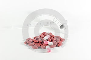 Dark red and pink pills spilling from a white Syringe. Focus at
