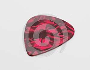 Dark red plastic guitar plectrum isolated on white background.