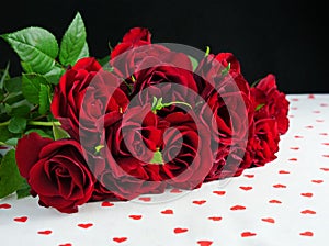 Dark red roses on a white table with red hearts over black background