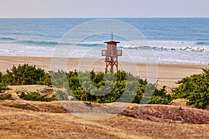 Dark red wooden lifeguard tower and empty sandy beach on the seashore in the off season