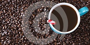 Dark roasted coffee beans background with blue filled coffee cup with peppermint