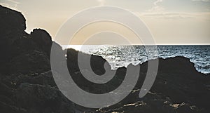 Dark rocks and stones on the Black Sea coast against which blue tidal waves beat in the backlight