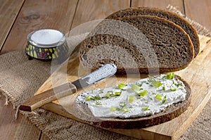 Dark rye bread, sandwich with cream and knife on wooden cutting board and salt in saltshaker on burlap. Close-up