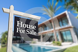 A dark for sale sign in front of a contemporary modern house with swimming pool. Real estate concept