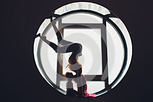 The dark silhouette of a beautiful woman with child on the background of the round window. yoga, acrobatics.