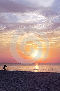 Dark silhouette of a child playing on the beach by sunset. Sea and pastel colours of sky and clouds. Magical sea landscape. Summer