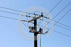 Dark silhouette of concrete electrical utility pole with multiple electrical wires connected over glass insulators on blue sky