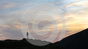 Dark silhouette of a hiker climbing a mountain at sunset reaching summit like a winner.
