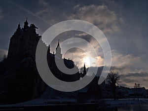 Dark silhouette of Hohenzollern Castle in Sigmaringen, Germany on the shore of Danube River in winter season with bright sun.