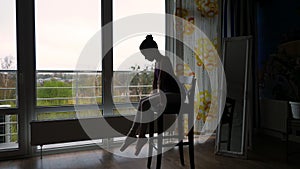 Dark silhouette of Little ballet dancer, girl in a ballet leotard, resting sitting on chair after practicing pointe