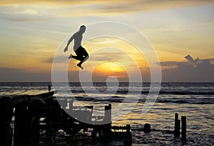 Dark silhouette of a man jumping into the water from a pier