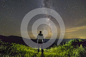 Dark silhouette of a man standing in mountains at night enjoying milky way view