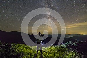 Dark silhouette of a man standing in mountains at night enjoying milky way view