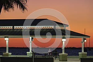 Dark silhouette of people resting under alcove roof on sea shore in public park at sunset