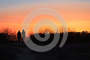 dark silhouettes of 2 people watch the orange sunset on the beach of RÃ¼gen on the Baltic Sea.