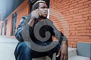 Dark-skinned annoyed man talking by mobile phone and sitting on concrete steps.