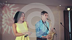 Dark-skinned black woman singer and thin saxophone player performing on stage.