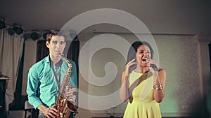 Dark-skinned black woman singer and thin saxophone player performing on stage.