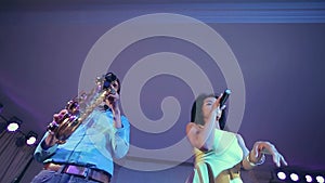 Dark-skinned black woman singer and thin saxophone player performing on stage.