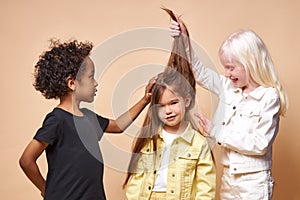 Dark-skinned boy and albino girl touching caucasian friend`s long hair