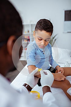 Dark-skinned doctor putting bright plaster on arm for little boy