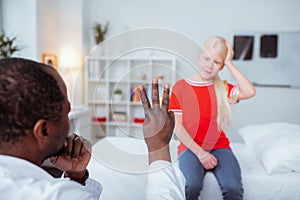 Dark-skinned doctor showing girl with concussion three fingers