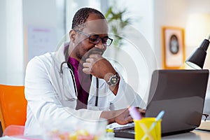 Dark-skinned doctor wearing glasses and watch feeling thoughtful