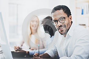 Dark skinned entrepreneur wearing glasses, working in modern office.African american man in white shirt looking and smiling at the photo