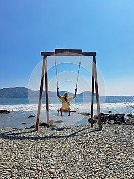 Dark-skinned Latino adult man with sunglasses, hat and shorts enjoys his vacation on the beach on a swing having fun and relaxing