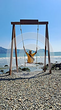 Dark-skinned Latino adult man with sunglasses, hat and shorts enjoys his vacation on the beach on a swing having fun and relaxing