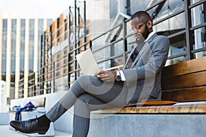 A dark-skinned man in a business suit is using a laptop outdoors. Digital education and remote work