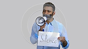 Dark-skinned man speaking in megaphone with taped mouth.