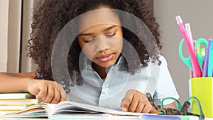 Dark-skinned schoolgirl reading a book doing homework