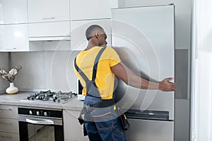 Dark-skinned service man in yellow tshirt repairing the fridge