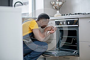 Dark-skinned service man in yellow tshirt repairing the gas stove