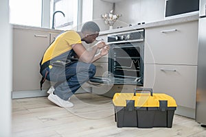 Dark-skinned service man in yellow tshirt repairing the gas stove