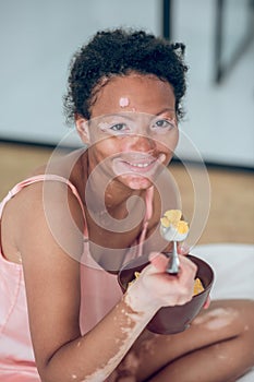 A dark-skinned woman eating cereals while sitting on bed