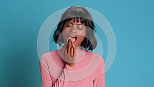 Dark skinned woman yawns with her mouth wide open on a background of blue wall.