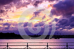 Dark sky with colorful clouds over water.