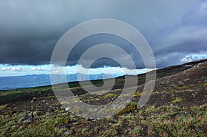 Dark slope of Villarrica volcano with sparse vegetation, low dark clouds