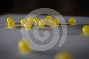 Dark soft focus close up of multiple small yellow balls candy BBs or pills on a gray paper with black background photo