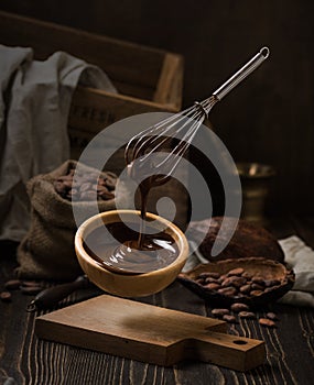 Dark still life with melted chocolate in wooden bowl