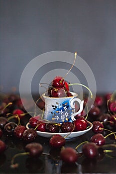 Dark stillife with porcelain cup of fresh cherries