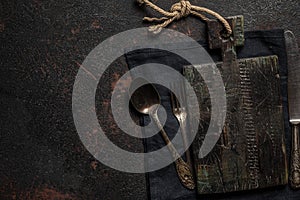 Dark stone kitchen table with old wooden cutting board, vintage cutlery and towel. Cooking background. Top view