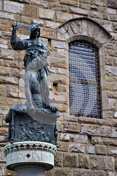 Dark stone statue depicting a woman with a sword holding by the hair of a man seated at his feet, in Florence.