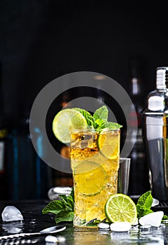 Dark and Stormy alcoholic cocktail drink with dark rum, ginger ale, lime and ice, black bar counter background