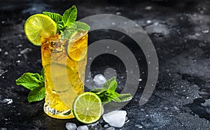 Dark and Stormy cocktail drink with dark rum, ginger ale, lime and ice with bottles, black bar counter background