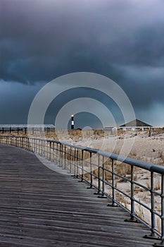 Dark stormy sky over a wooden boardwalk leading to a lighthouse. Fire Island