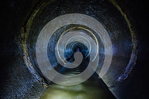 Dark underground sewer round concrete tunnel. Industrial wastewater and urban sewage flowing throw sewer pipe